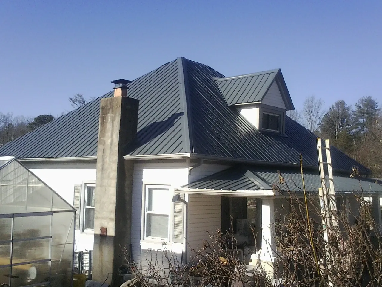 Dark blue standing seam metal roof on a white farmhouse with dormer — Slate & Tile Roof Repair by Roofing Brothers in Leigh