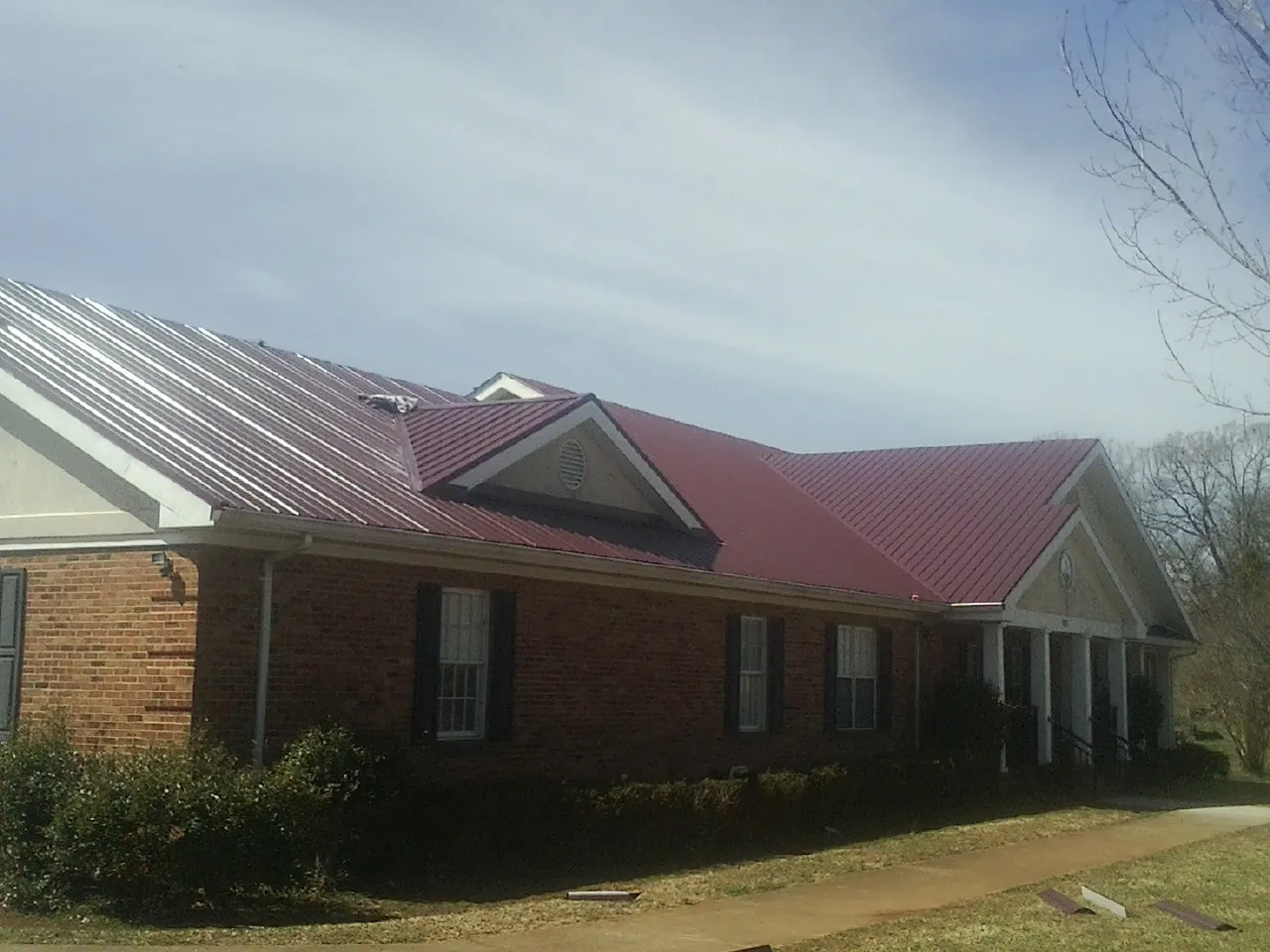 Red metal roof with gabled entries on a long brick building, from a Hail Damage Roof Repair job in Leigh