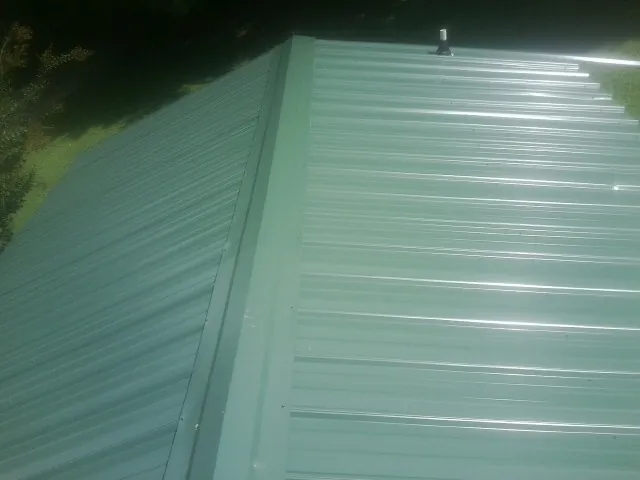 New green metal panels meeting at the ridge of a roof — Flat Roof Repair work by our crew in Leigh
