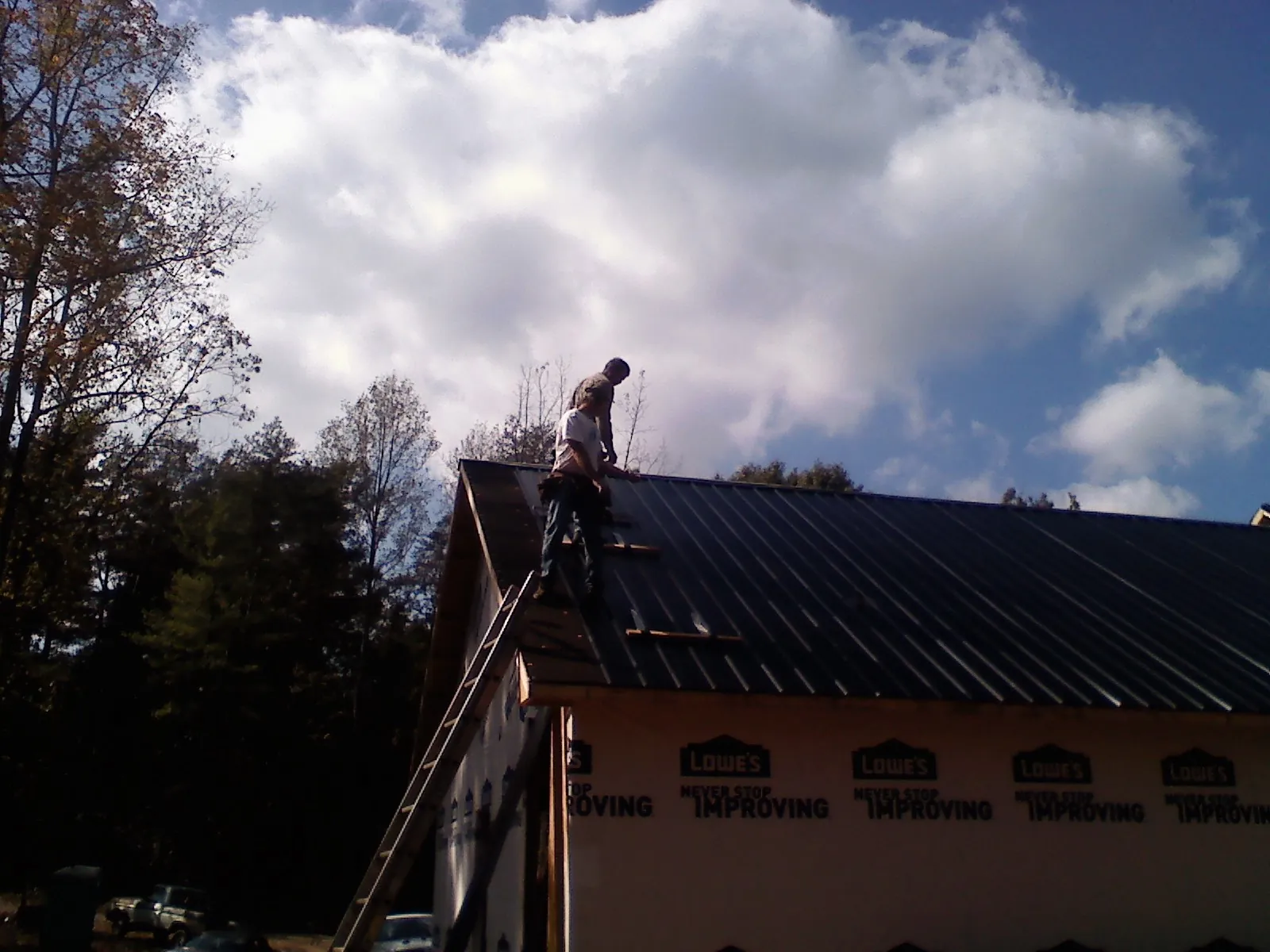 Roofer fastening dark metal panels high against a cloudy sky, from a Roof Inspection job in Leigh
