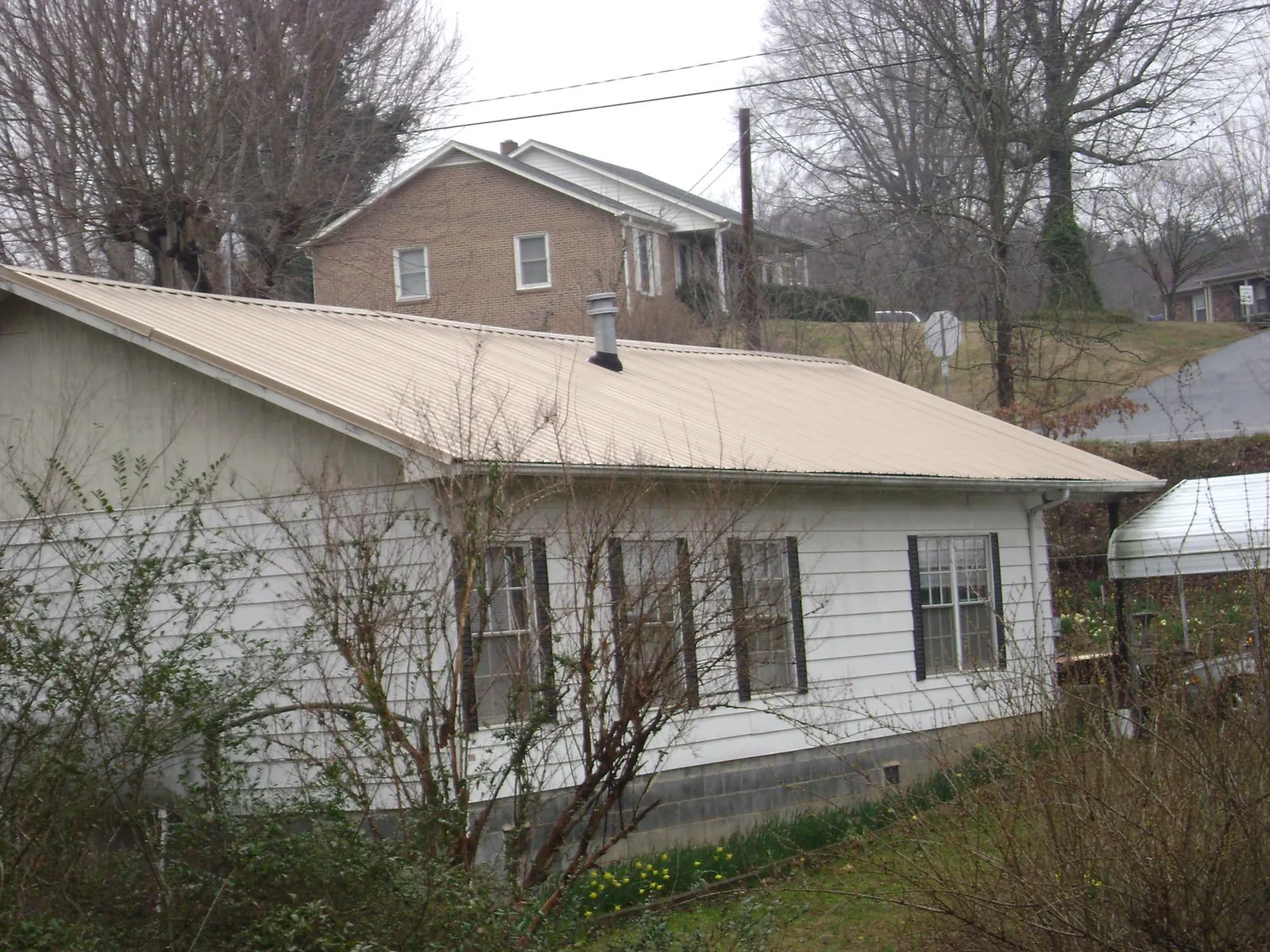 Tan metal roof on a white sided house set into a hillside — Commercial Roofing by Roofing Brothers in Leigh
